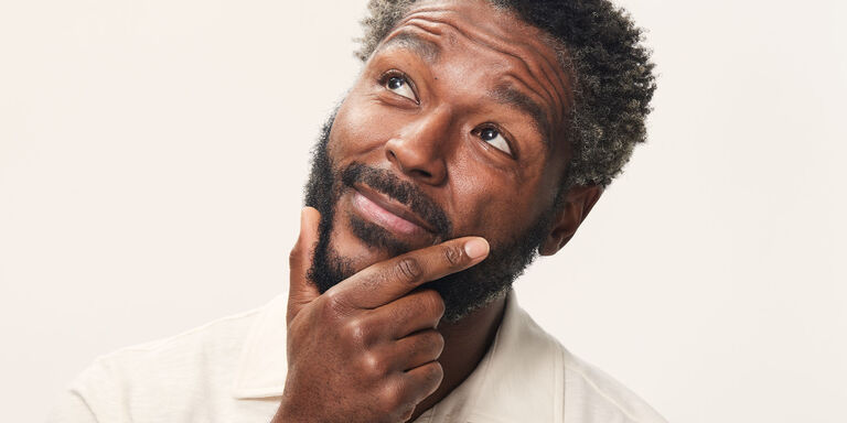 Close-up of individual in neutral attire with hand on chin, on white background.