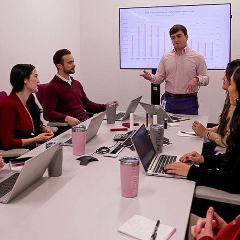 Team gathered in a conference room with laptops while someone presents data charts on a screen