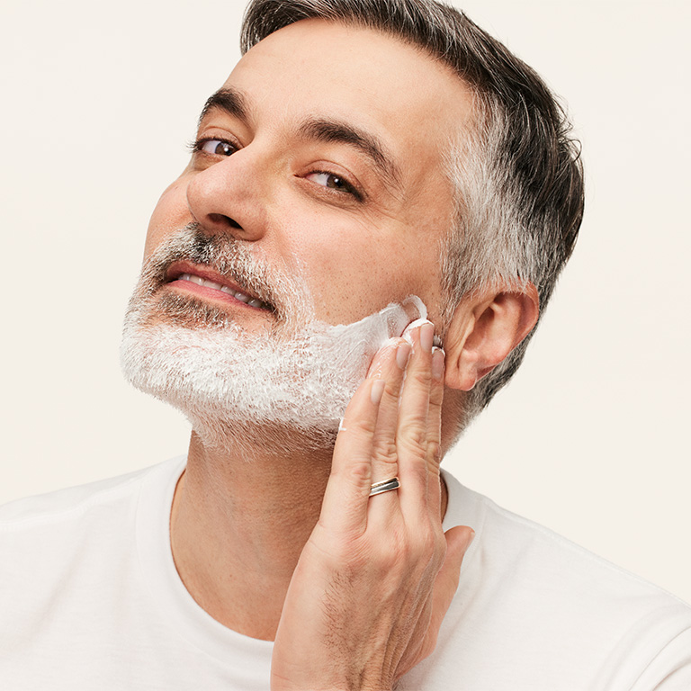 Person wearing a plain white crew-neck shirt applying shaving cream.